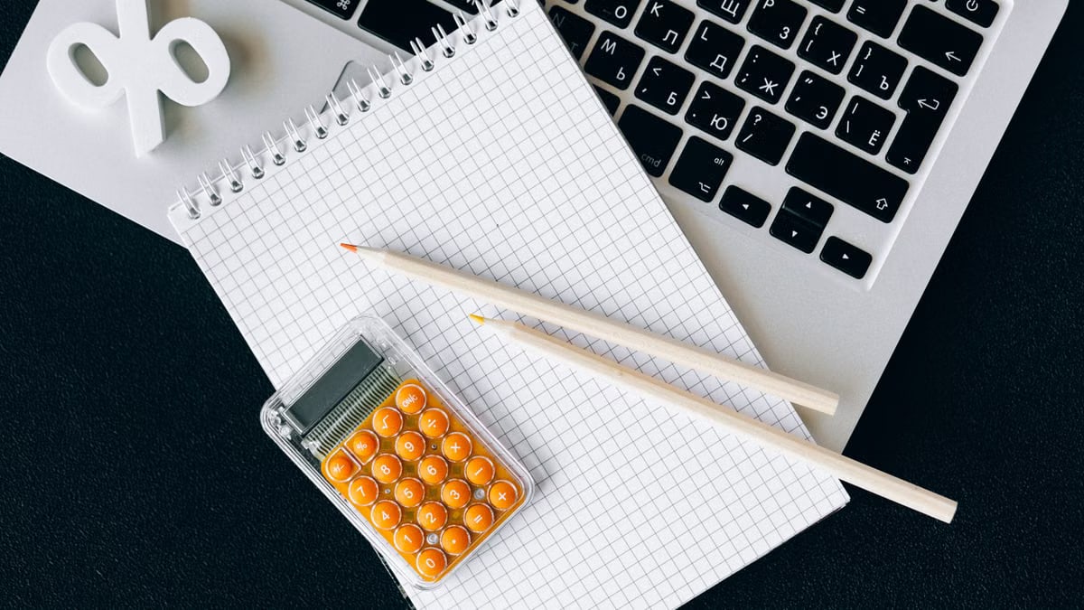 Flat lay of office supplies including a calculator and notebook on a laptop desk.