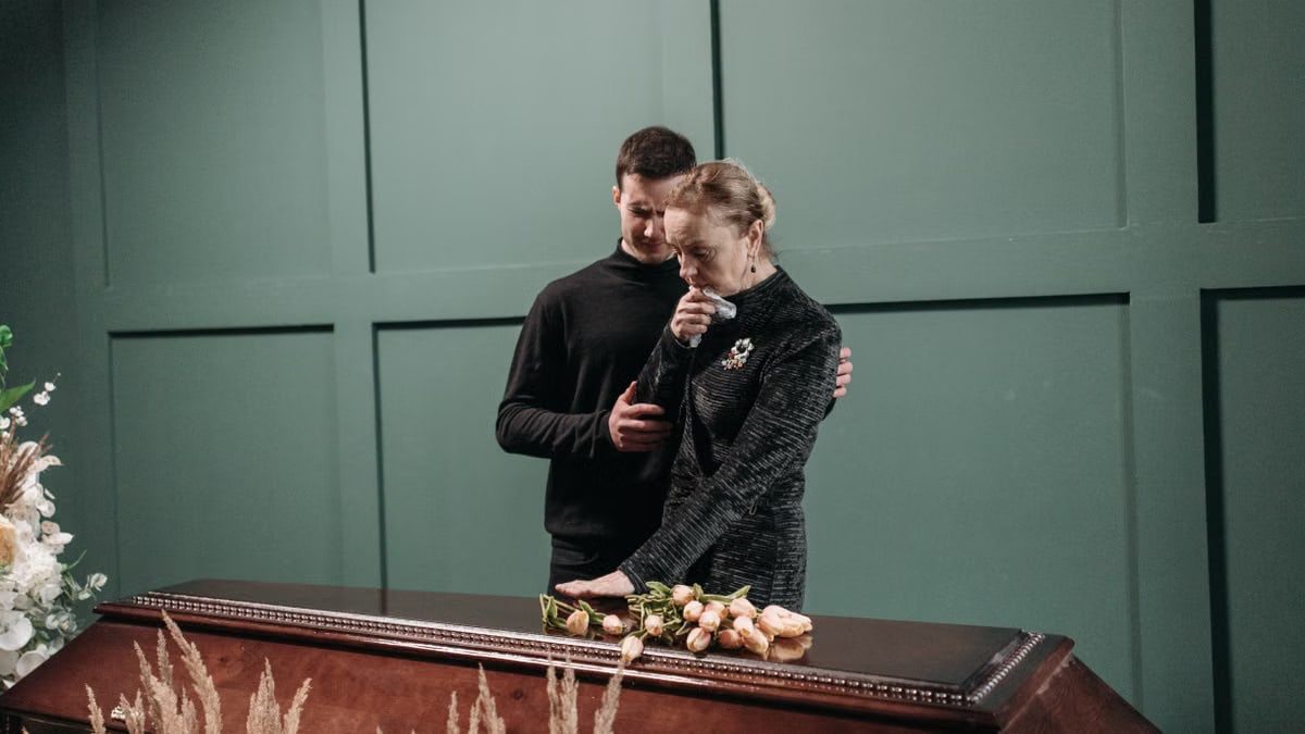 Grieving family members stand solemnly beside a coffin during a funeral.